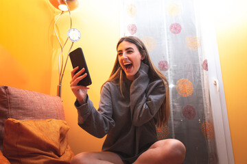 Young caucasian woman with a laughing while using a smartphone in the living room.
