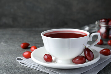 Cup of fresh dogwood tea and berries on grey table. Space for text
