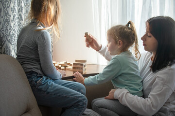 Three sisters of different ages play the board game , they lay out together wooden sticks together, in a cozy family environment