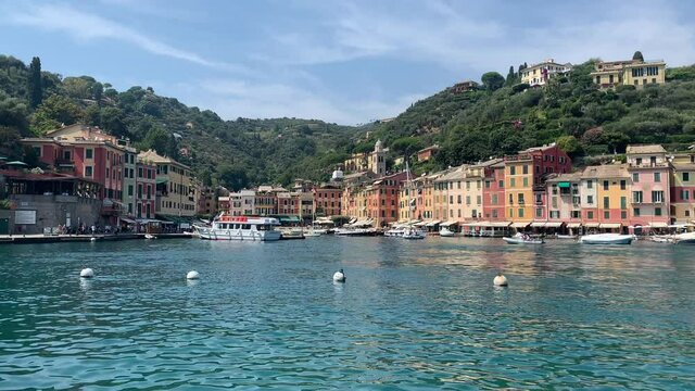 Skyline of Portofino village with colourful  houses and boat sailing in emerald water. It is famous holiday resort and fishing Italian riviera town. Portofino, Liguria, Italy