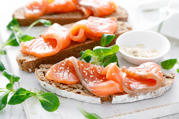 Whole grain rye bread open sandwiches with salted salmon on a white rustic wooden table. Healthy food