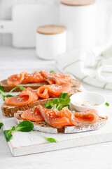 Whole grain rye bread open sandwiches with salted salmon on a white rustic wooden table. Healthy food