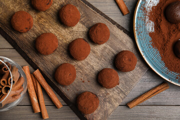 Delicious chocolate truffles with cocoa powder and cinnamon on wooden table, flat lay