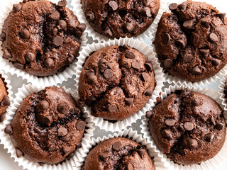 Chocolate muffins in white baking paper cup from above. Close-up of brown cupcakes with chocolate drops. Top view, flat lay