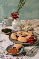 Still life of: pies with meat, pasta from beet leaves, nuts, hot sauce on large and small plates. Viburnum in a vase. Linen tablecloth.