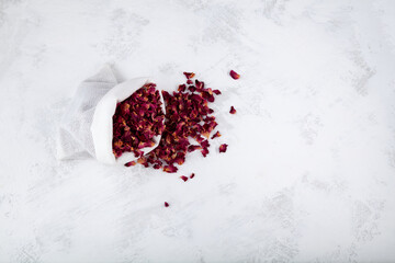 Dried rose petals in white pouch on light textured background. Selective focus, copy space. Purple rose flowers for fragrant flower tea, sachets and aromatic compositions