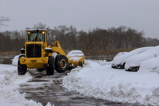 Road maintenance of tractor removing snow on parking lot for car after snowfall