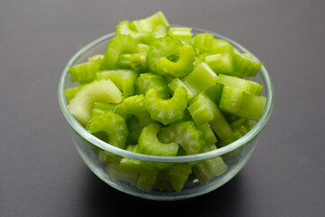 Fresh celery in glass bowl on dark background.