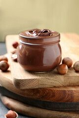 Glass jar with tasty chocolate hazelnut spread and nuts on wooden board