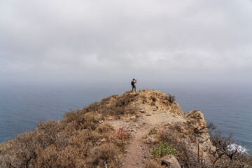 A lone tourist photographer stands on a mountain, against the backdrop of the ocean. Tenerife. Canary Islands. Spain.