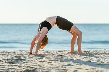 Woman doing the bridge position of yoga on a beach