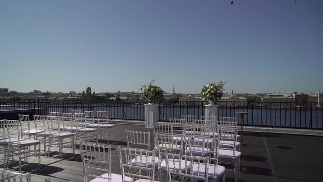 Decorated wedding ceremony outside in summer on rooftop. Wedding arch with white and pink rose flowers. White Chiavari chairs.