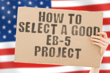 The phrase " How to select a good EB-5 project " on a banner in men's hand with blurred Russian flag on the background. Technology. Startup. Business. Internet. Idea. Smart. Step. Strategy