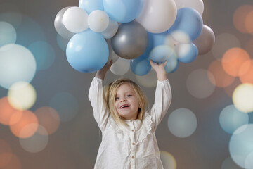 Studio portrait of happy little girl holding a group of white and blue balloon. Concept of celebration, happiness, wishes and hopes.