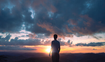 silhouette of a young man with the clouds and sunset in the background.