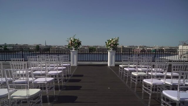 Decorated wedding ceremony outside in summer on rooftop. Wedding arch with white and pink rose flowers. White Chiavari chairs.