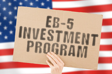 The phrase " EB-5 investment program " on a banner in men's hand with blurred Russian flag on the background. Startup. Investing. Finance. Venture. Fund. Businessperson. Plan. Invest