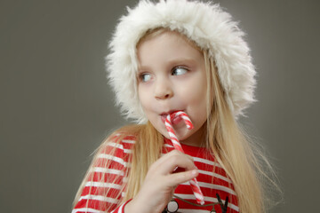 Studio portrait of 4 years old girl in Santa hat holding candy cane. It's holiday season!
