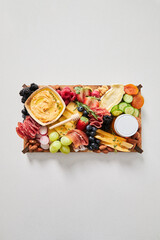 Top view of a cheese board with hummus, fruit and vegetables on a white background