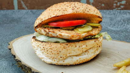 Close-up of tasty chicken burger with french fries, lettuce, tomato and cucumber pickle on a natural wooden tray	front of vintage brick wall