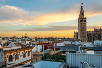Sunset view from a rooftop overlooking the Andalusian city of Seville, Spain, with the Giralda Tower and the great Seville Cathedral in view over the skyline at early evening.