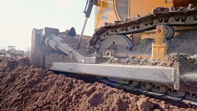 Tracking shot of crawler bulldozer working on construction site or quarry. Mining machinery moving clay, smoothing gravel surface for new road. Earthmoving, excavations, digging on soils.