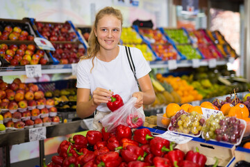 Pretty young woman purchaser choosing fresh organic pepper in a grocery store