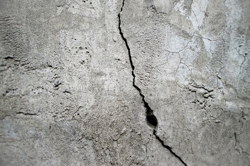 Vertical crack on the wall with a hole. Concrete old surface with grainy texture.