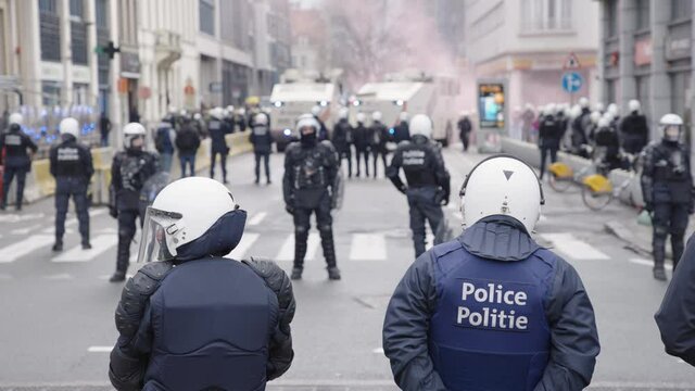 Belgian police line both sides of the street in full riot gear during protest, slow motion
