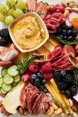 Top view of a cheese board with hummus, fruit and vegetables on a white background
