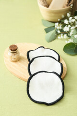 Wooden board with reusable cotton pads and bottle of sea salt on color background