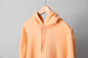 Stylish peachy hoodie near light wall, closeup