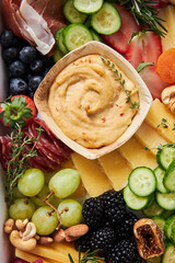 Top view of a cheese board with hummus, fruit and vegetables