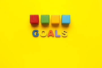 Different color wooden cubes and word GOALS on yellow background