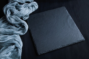 Black slate board on top view of dark stone texture with gray gauze tablecloth.