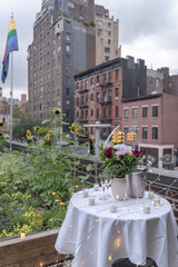 A bouquet of flowers sits on top of a table draped with white tablecloth, candles and fairy lights in celebration of a surprise proposal. Buildings in West Villages are in the background.