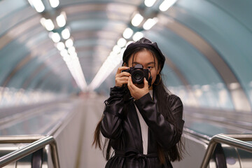 Asian tourist girl make photos while travelling. Young chinese female hold camera riding on escalator. Professional photographer or traveler take picture of public transport. Photography hobby concept