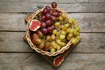 Wicker basket with sweet grapes and fig on wooden background