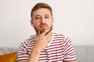 Thoughtful young man in earphones at home