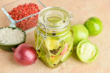 Jar with canned green tomatoes and fresh vegetables on beige background