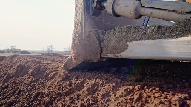 Tracking shot of crawler bulldozer working on construction site or quarry. Mining machinery moving clay, smoothing gravel surface for new road. Earthmoving, excavations, digging on soils.