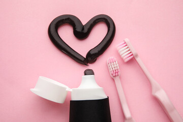 Heart made of black tooth paste, brushes and tube on pink background