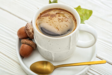 Cup of coffee with acorns on light wooden background, closeup