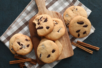 Fototapeta na wymiar Board with tasty homemade cookies and cinnamon on dark background
