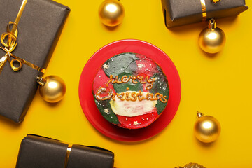 Plate with tasty bento cake, gifts and Christmas balls on yellow background