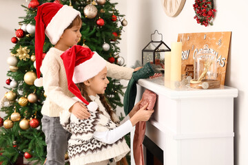Cute little children hanging Christmas socks on fireplace in living room
