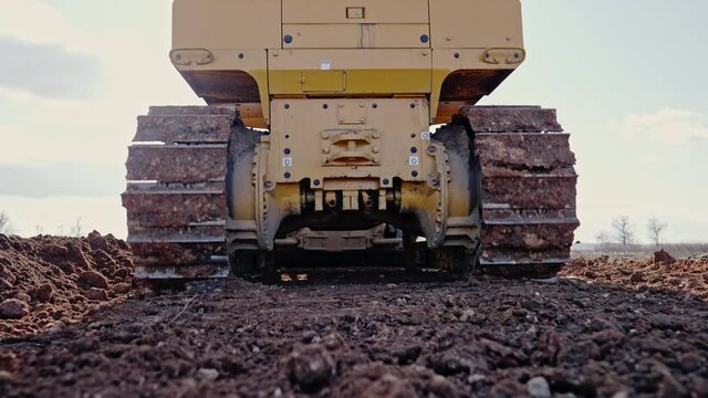 Tracking shot of crawler bulldozer working on construction site or quarry. Mining machinery moving clay, smoothing gravel surface for new road. Earthmoving, excavations, digging on soils.