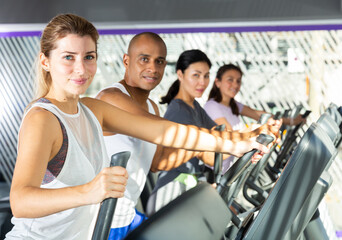 Portrait of sporty young adult woman doing cardio workout on elliptical cross trainer at fitness...