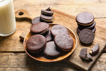 Plate with tasty chocolate cookies and glass of milk on wooden background