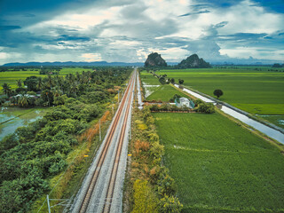 Electrified railway tracks surrounded by green paddy field in malaysia during overcast day